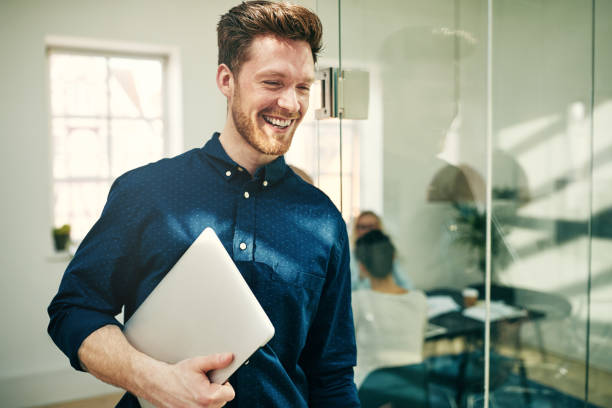 istock Laughing young businessman walking with his laptop at work 1009561622