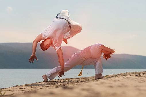 Men train capoeira on the beach - concept about people, lifestyle and sport. Training of two fighters