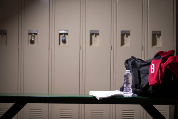 Generic sports equipment in school gymnasium locker room. Various sports equipment on bench inside high school or college gymnasium locker room.   Items include:  sports jersey, water, towel, gym bag.. locker room stock pictures, royalty-free photos & images