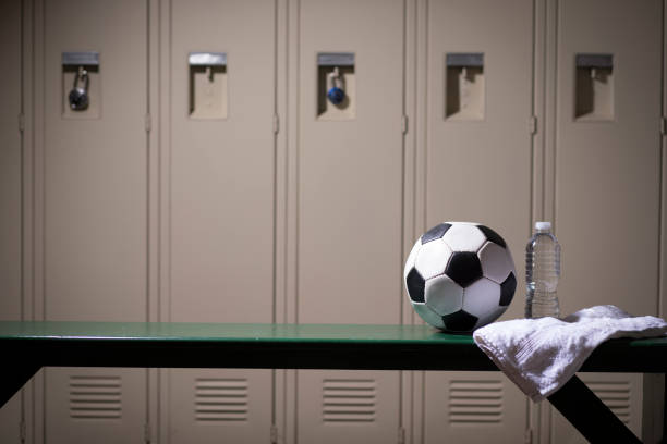 Soccer sports equipment in school gymnasium locker room. Various sports equipment on bench inside high school or college gymnasium locker room.   Items include: soccer ball, water bottle, towel. locker room stock pictures, royalty-free photos & images