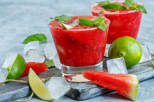 Glasses of watermelon Mojito, slices of lime, mint and ice on the serving board.