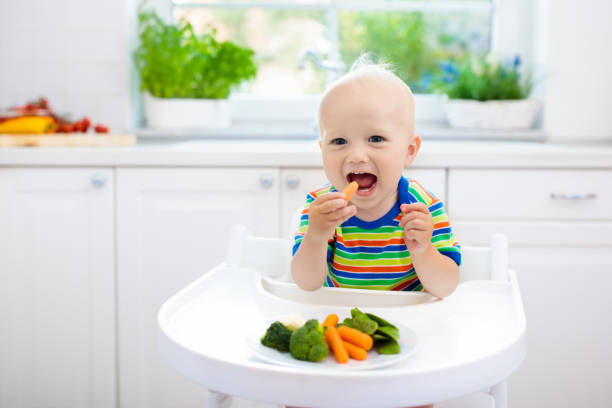 bébé mangeant des légumes dans la cuisine. alimentation saine. - baby food photos et images de collection