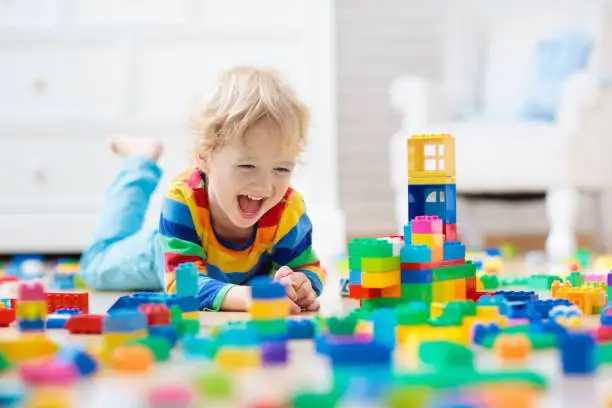 Child playing with colorful toy blocks. Little boy building tower at home or day care. Educational toys for young children. Construction block for baby or toddler kid. Mess in kindergarten play room.