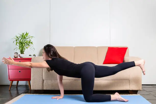 Beautiful caucasian brunette woman in black clothes on blue yogamat doing bird-dog pose