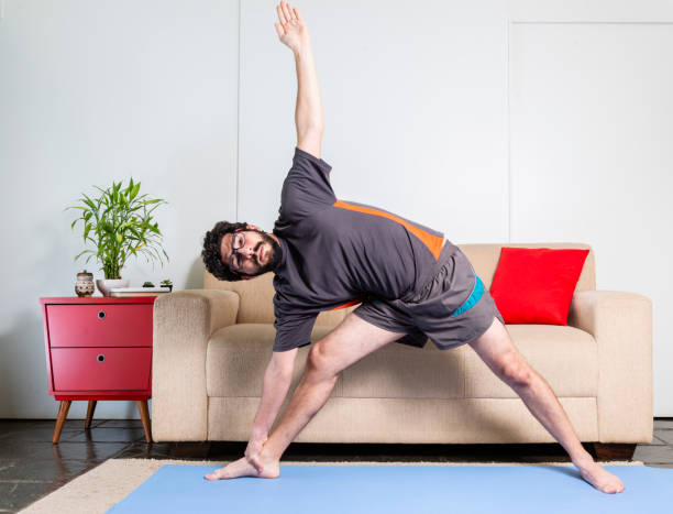 istock Beautiful caucasian bearded man in black clothes on blue yogamat doing triangle pose 1009597208