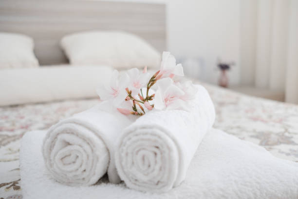 White And Fresh Laundered Fluffy Towels With Flower On Bed In