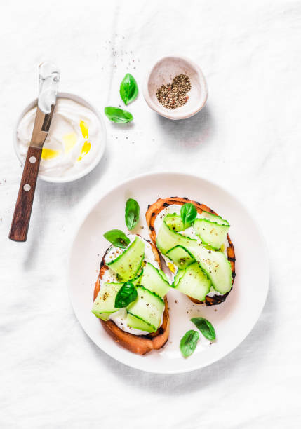 istock Labne and pickled cucumbers toast on a light background, top view. Sandwiches with soft cheese and cucumber - delicious healthy breakfast, snack. Flat lay 1009600502