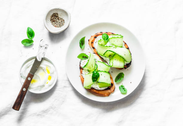 Labne and pickled cucumbers toast on a light background, top view. Sandwiches with soft cheese and cucumber - delicious healthy breakfast, snack. Flat lay