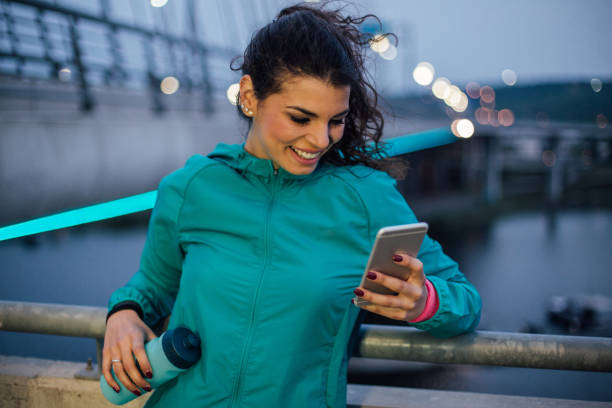 istock Happy woman holding bottle of water while using mobile phone 1009604078