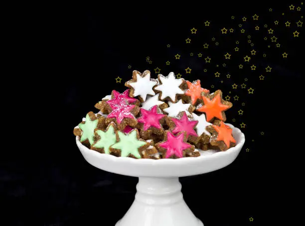christmas biscuit cinnamon stars with colored glaze against black background with golden stars