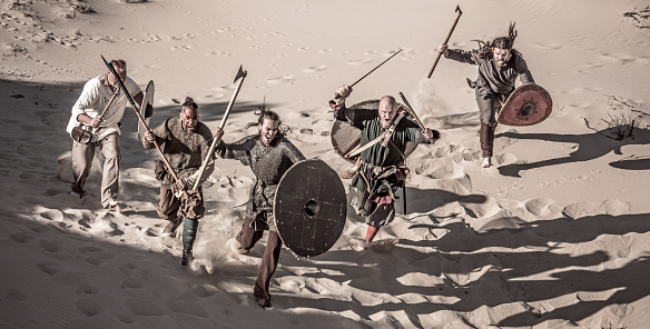 A hoard of Weapon wielding viking warriors on a sandy battlefield dune