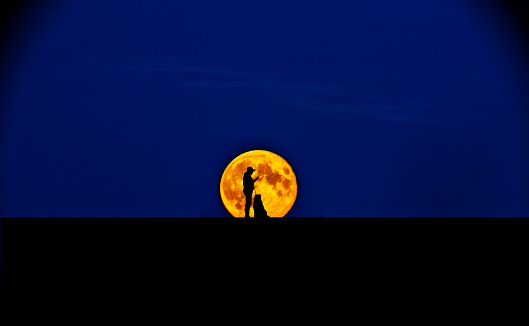 Silhouette of woman and border collie against blood moon rising behind hill