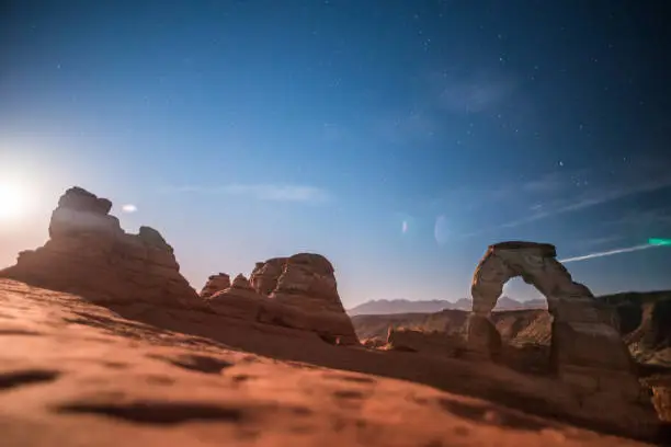 A night time photo taken of Delicate Arch in Utah USA. Lens flare from the light of the full moon intentional and adds a cinematic effect.