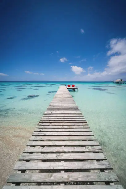 Endless wooden jetty into turquoise lagoon under blue summer sky. Tuamotu Atoll Group, French Polynesia
