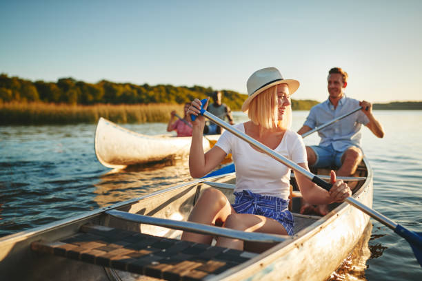 Laughing young woman canoeing on a lake with friends Young woman laughing while paddling a canoe on a lake with her boyfriend and another couple on a sunny summer afternoon canoeing stock pictures, royalty-free photos & images
