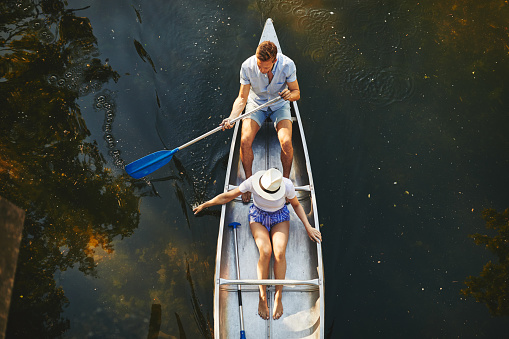High angle of a young couple sitting in a canoe together paddling on a still lake in summer