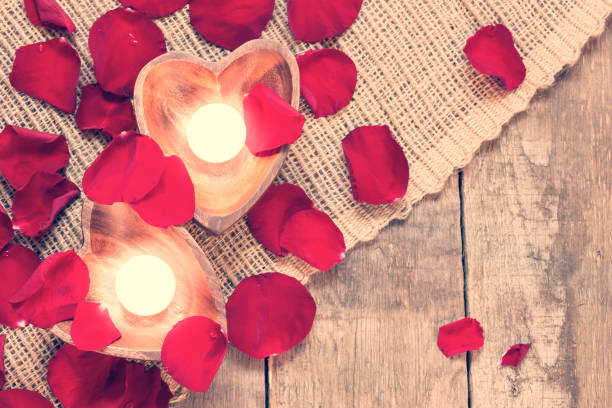 istock Two enlightened candles in heart-shaped candleholders with rose petals 1009739060