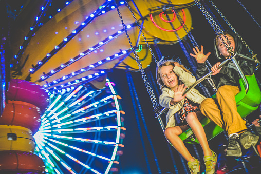 Two cute kids on a carnival ride, a big swing, in the evening, enjoying themselves at the fair