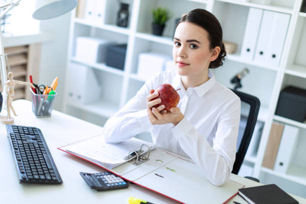 istock Young girl in the office working with documents and holding an apple. 1009739362