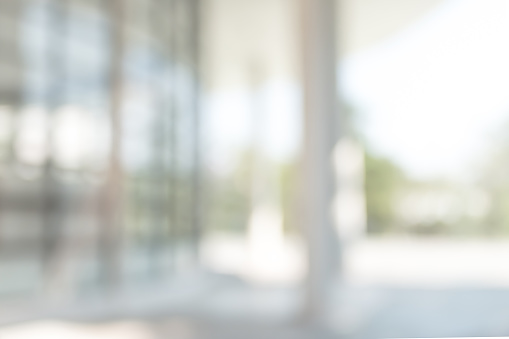 Office or university building blur background exterior view with blurry empty lobby space, entrance hall glass wall window and light bokeh