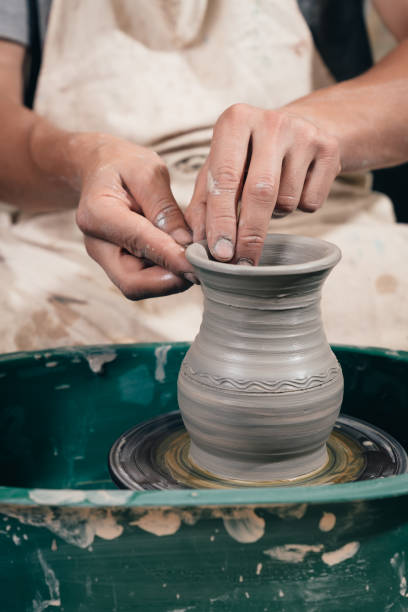 istock Young man making ceramic pot on the pottery wheel. Creating potter working on the wheel shaping clay making vase. 1009743220