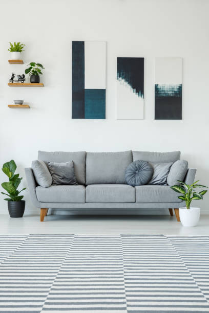 istock Posters above grey settee in bright living room interior with plants and patterned carpet. Real photo 1009764552