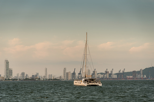 Sailboat boat anchored Cartagena at dusk with commercial port and modern city background. Colombia