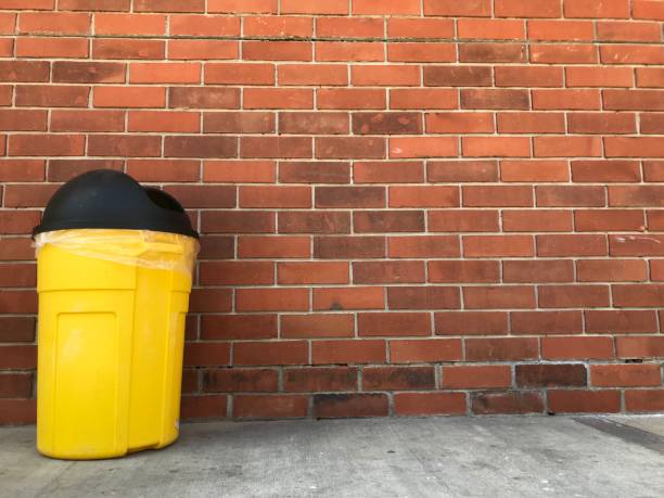 istock Yellow trash bin with black cap in front of a brick wall 1009822258