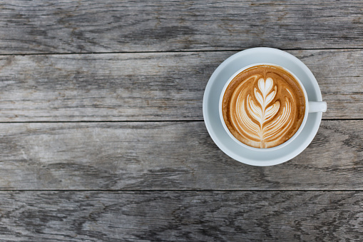 A beautiful cup of cappuccino with latte art in the wooden space background. Trendy toning. Minimal composition, hipster vibes. Top view, flat lay copy space for your text.