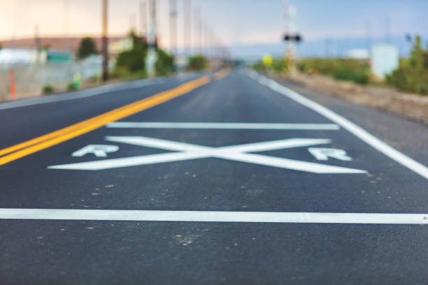 istock Rural Paved Road Background with White Railroad Crossing Warning Markers 1009841410