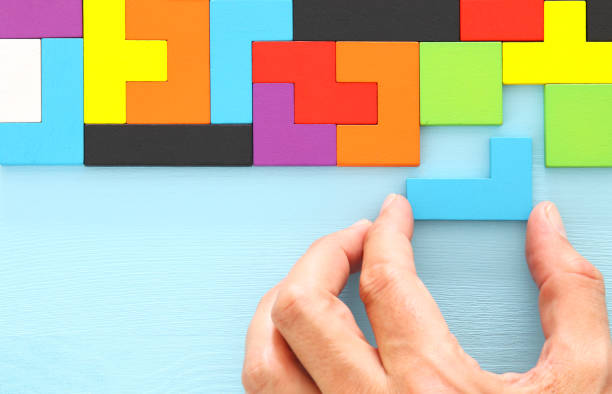 istock man's hand holding a square tangram puzzle, over wooden table. 1009844116