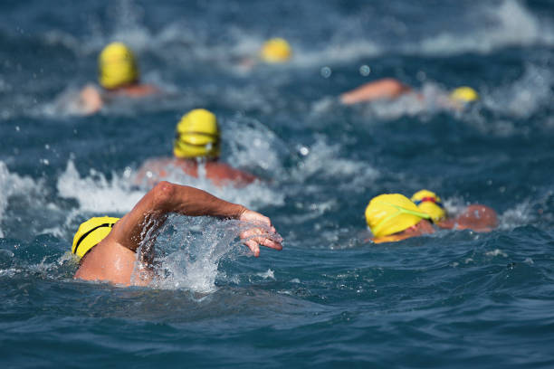 A group of young children wearing colorful swim caps participating in a swimming class in an indoor pool. The kids are lined up near the edge of the pool, preparing for swimming practice. Motion blur emphasizes the energetic atmosphere of the scene. Faces are unrecognizable and identities are not discernible. No model release required