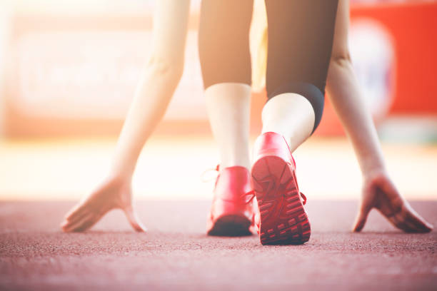 Female runner crouches into the starting position for sprint on running path.