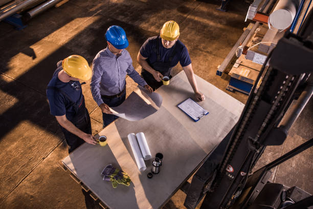 istock Above view of manual workers cooperating with an inspector while examining blueprints in a warehouse. 1009864880