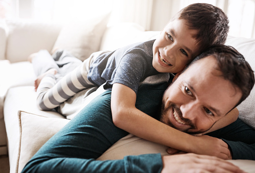 Shot of an adorable little boy having fun with his father on the sofa at home