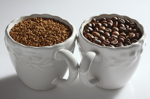 Fried coffee beans in a white cup on a neutral background