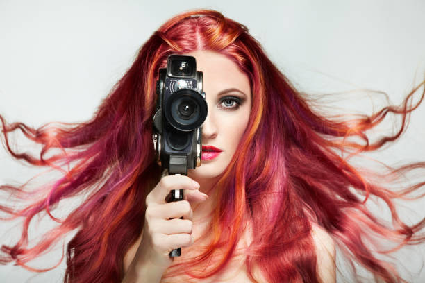 Beautiful Young Woman using a Retro Video Camera. Dyed Hair. Girl with perfect Makeup and Hairstyle. Model with perfect Healthy Dyed Hair. Pink Hairstyles