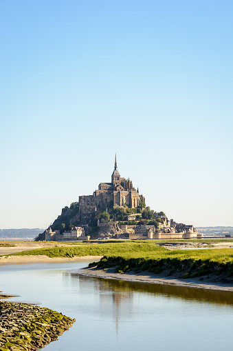View of the Mont Saint-Michel tidal island, located in France on the limit between Normandy and Brittany, at high tide with the Couesnon river in the foreground.