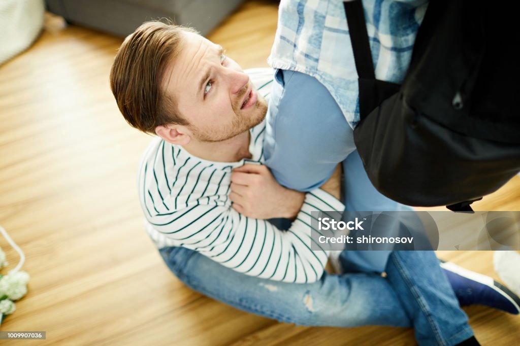 Please do not leave Young man begging his wife to stay with him while sitting on the floor and hugging her leg Men Stock Photo
