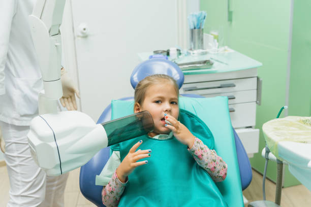 Child with a mother at a dentist's reception. The girl lies in the chair, behind her mother. The doctor works with an assistant. Procedure for drilling a tooth. Setting a temporary seal. stock photo