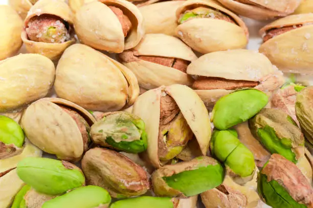 Background of the roasted salted pistachio nuts peeled from shells and nuts with partly open shells close-up at selective focus