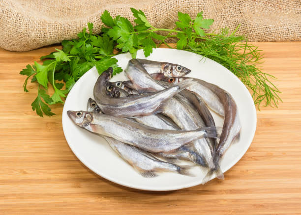 istock Defrosted uncooked capelins on the white dish and greens 1009913546