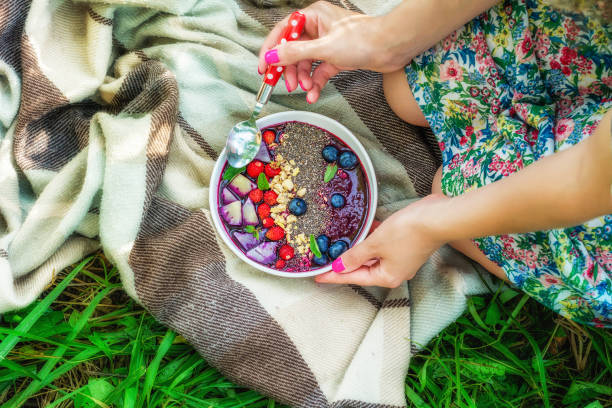 Woman holding smoothie bowl Woman seatting on the checked blanket and holding smoothie bowl. Picnic in the garden concept. Top view eating chia seeds stock pictures, royalty-free photos & images