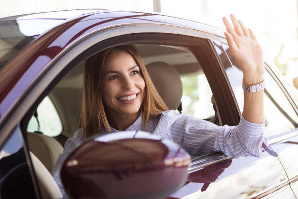 istock Young woman waving from a new car 1009914096