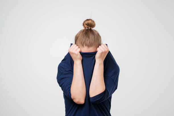 European woman hiding face under the clothes. She is oulling sweater on her head. European woman hiding face under the clothes. She is oulling sweater on her head. Depressed emotion. Wish to be alone. blame stock pictures, royalty-free photos & images
