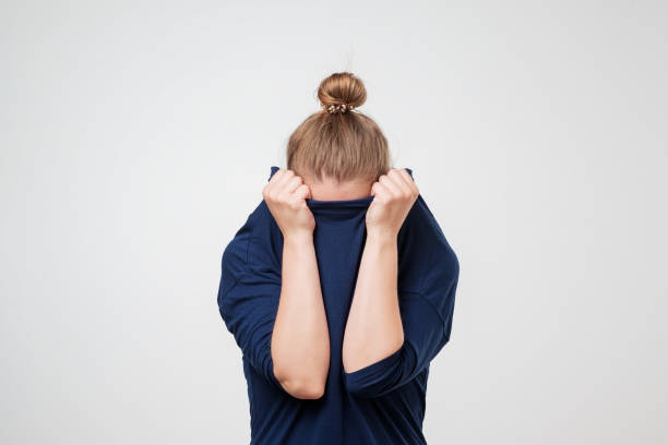 European woman hiding face under the clothes. She is oulling sweater on her head. European woman hiding face under the clothes. She is oulling sweater on her head. Depressed emotion. Wish to be alone. fearfull stock pictures, royalty-free photos & images