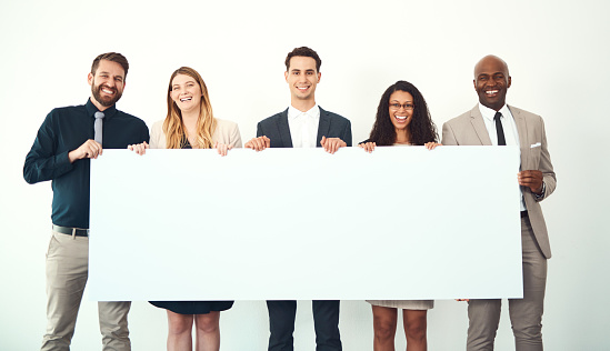 Cropped portrait of a group of business colleagues holding up a blank placard while standing in their office