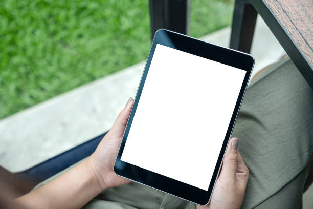 istock Top view mockup image of woman's hands holding black tablet pc with white blank screen while sitting in cafe with green nature background 1009942398