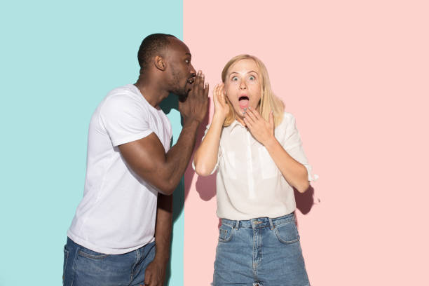 istock The young couple whispering a secret behind her hand over studio background 1009948288