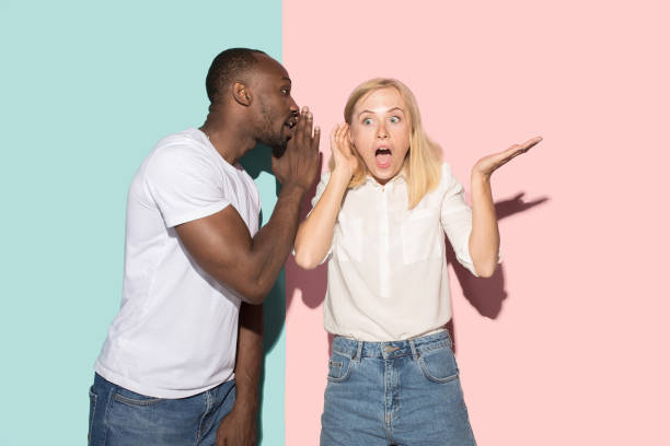istock The young couple whispering a secret behind her hand over studio background 1009948410